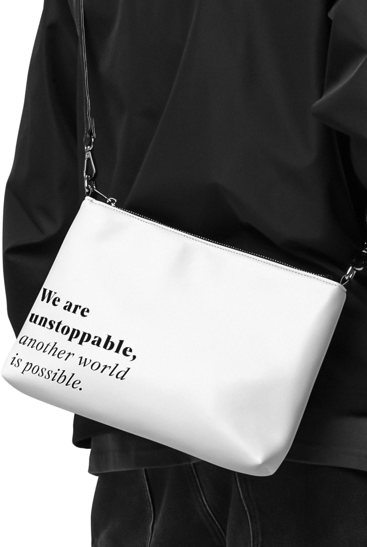 Person with dark clothing, wearing a white faux-leather purse or 
          crossbody bag for climate activists with the sentence 'We are unstoppable, another world is possible.' printed on it in black serif letters