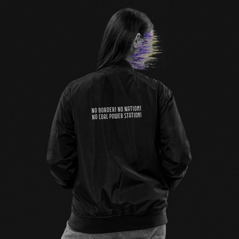 Woman turns her back, wearing a black bomber jacket made of recycling polyester, on the upper back of the bomber jacket, there is an embroidery saying 'No border! No nation! No coal power station!', the woman's face is made unrecognizable through colorful glitches