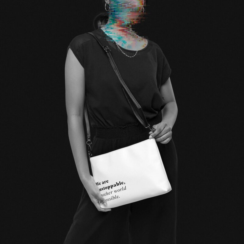 Woman with darkhair and a dark jumsuit, a white faux-leather purse for climate activists, with the sentence 'We are unstoppable, another world is possible.' printed on the lower left corner in serif letters, her face is made unrecognisable with colourful glitches