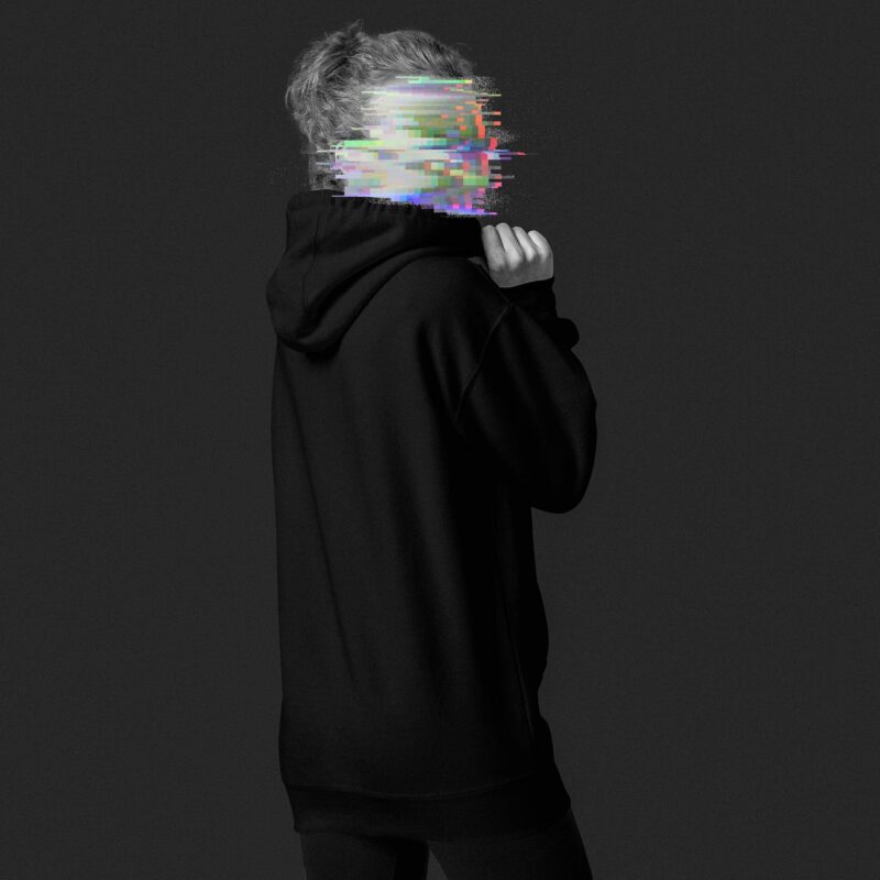 Sideview of a woman, wearing a black hoodie, her face is made unrecognisable through colourful glitches